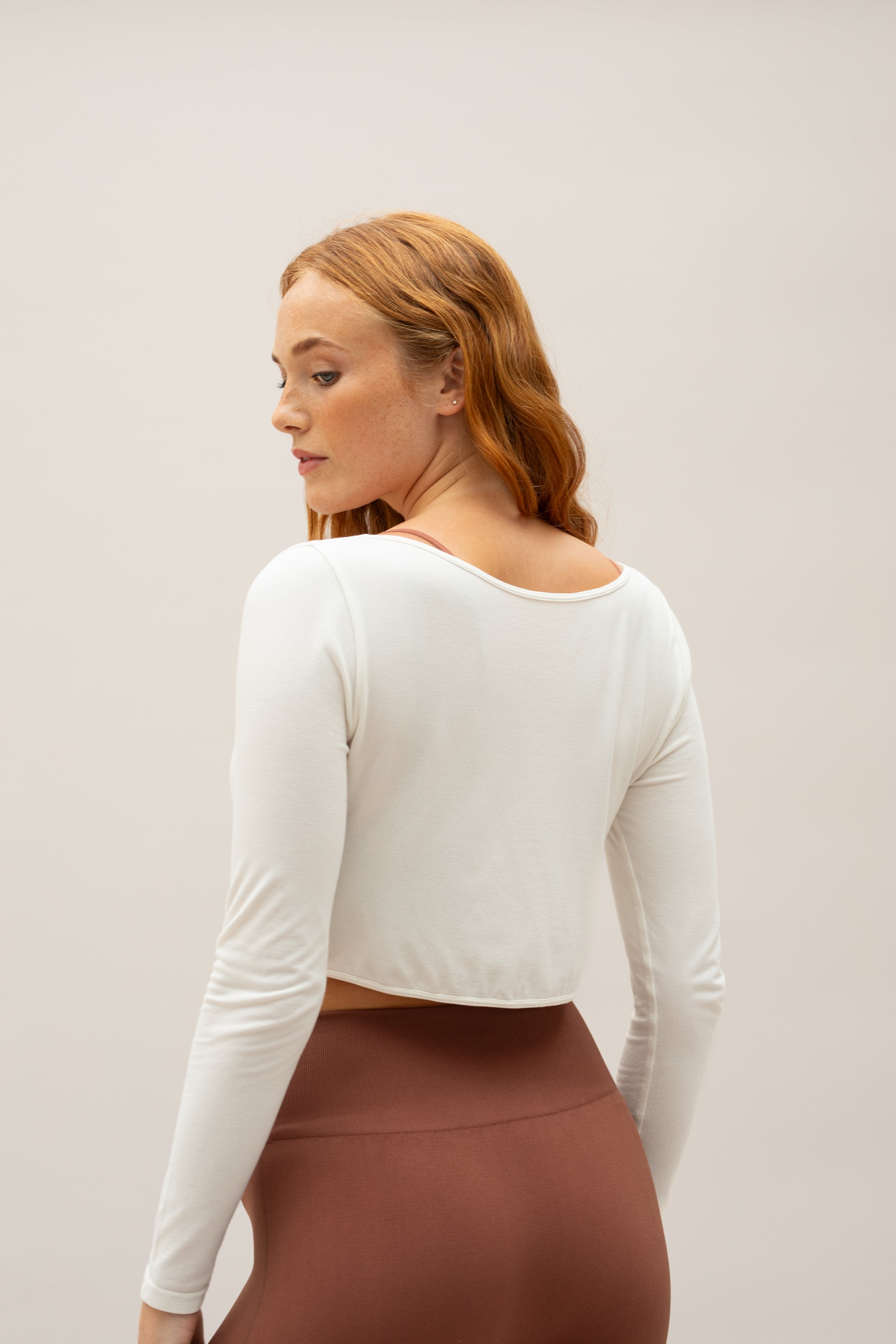 White cropped long sleeve white twisted front top with brown high waist leggings by sustainable women's activewear brand, Jilla. 