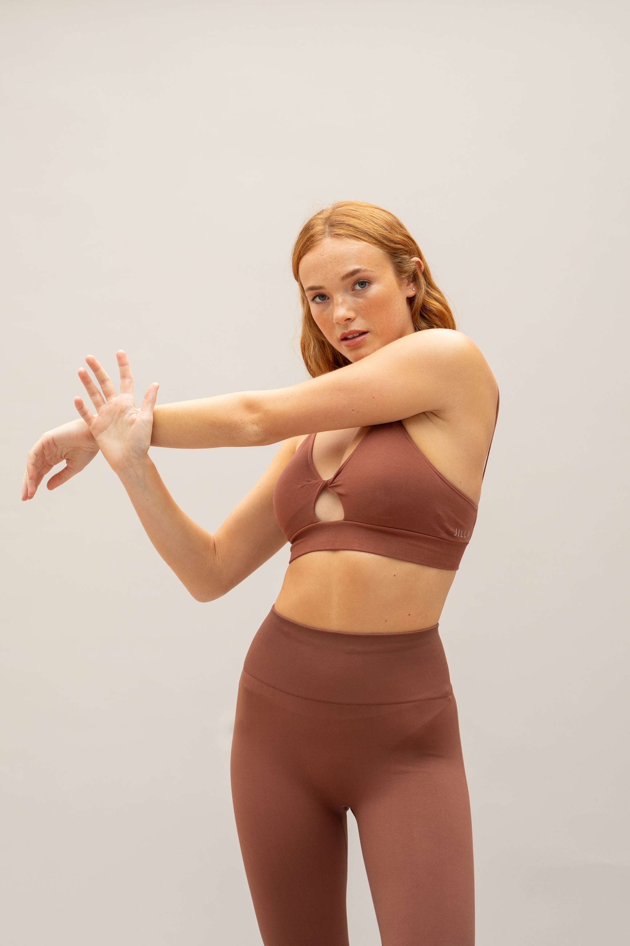 Brown supportive twisted from sports bra and brown high waisted flare leggings from sustainable activewear brand, Jilla. 